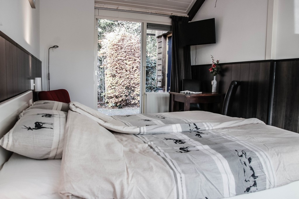 bed met op achtergrond open deur naar plaatsje, televisie in de hoek